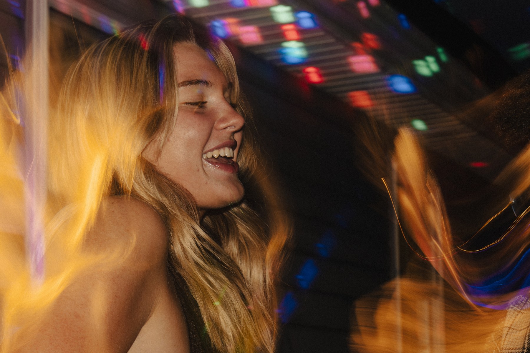 Alysa laughing in warm light with colorful nighttime light trails around her