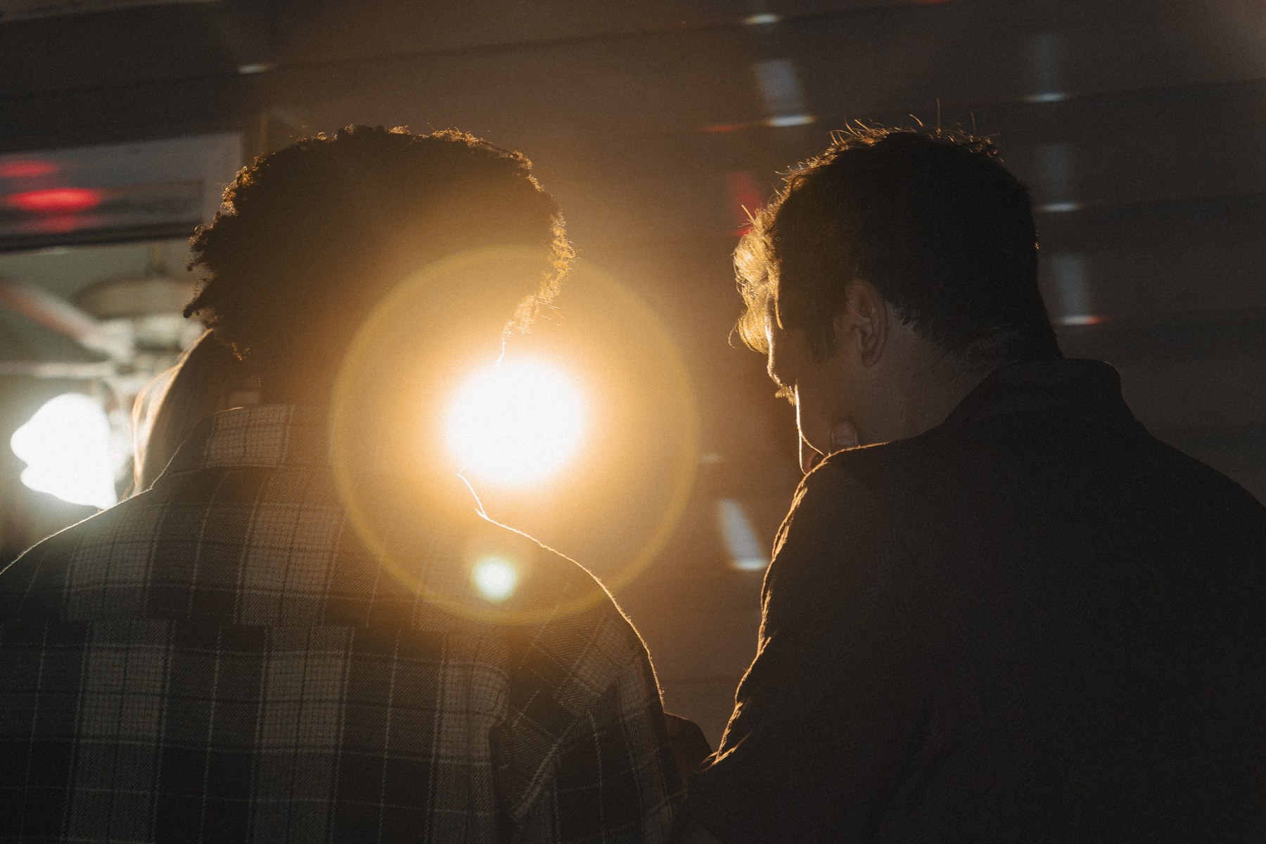 A bright warm light shining between Keion and another guest, outlining them against the darker room
