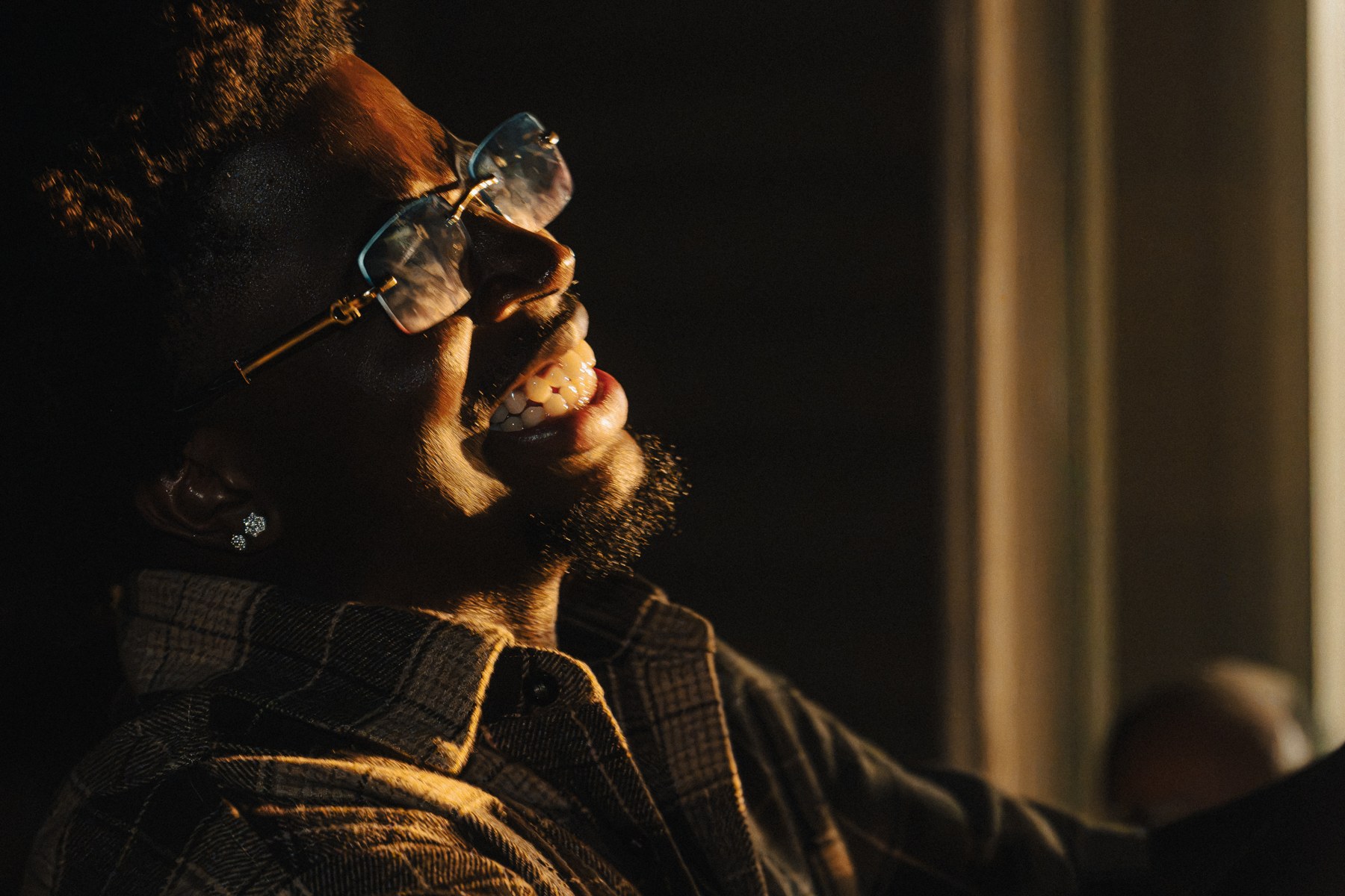 A close nighttime portrait of Keion with warm light catching his face and glasses against deep shadow