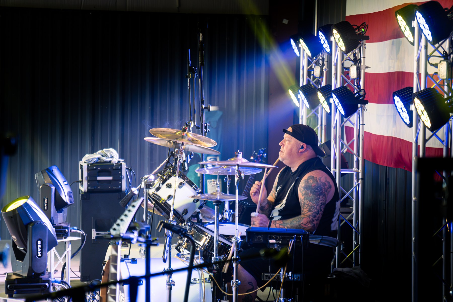 Drummer playing behind a kit with a flag in the stage backdrop