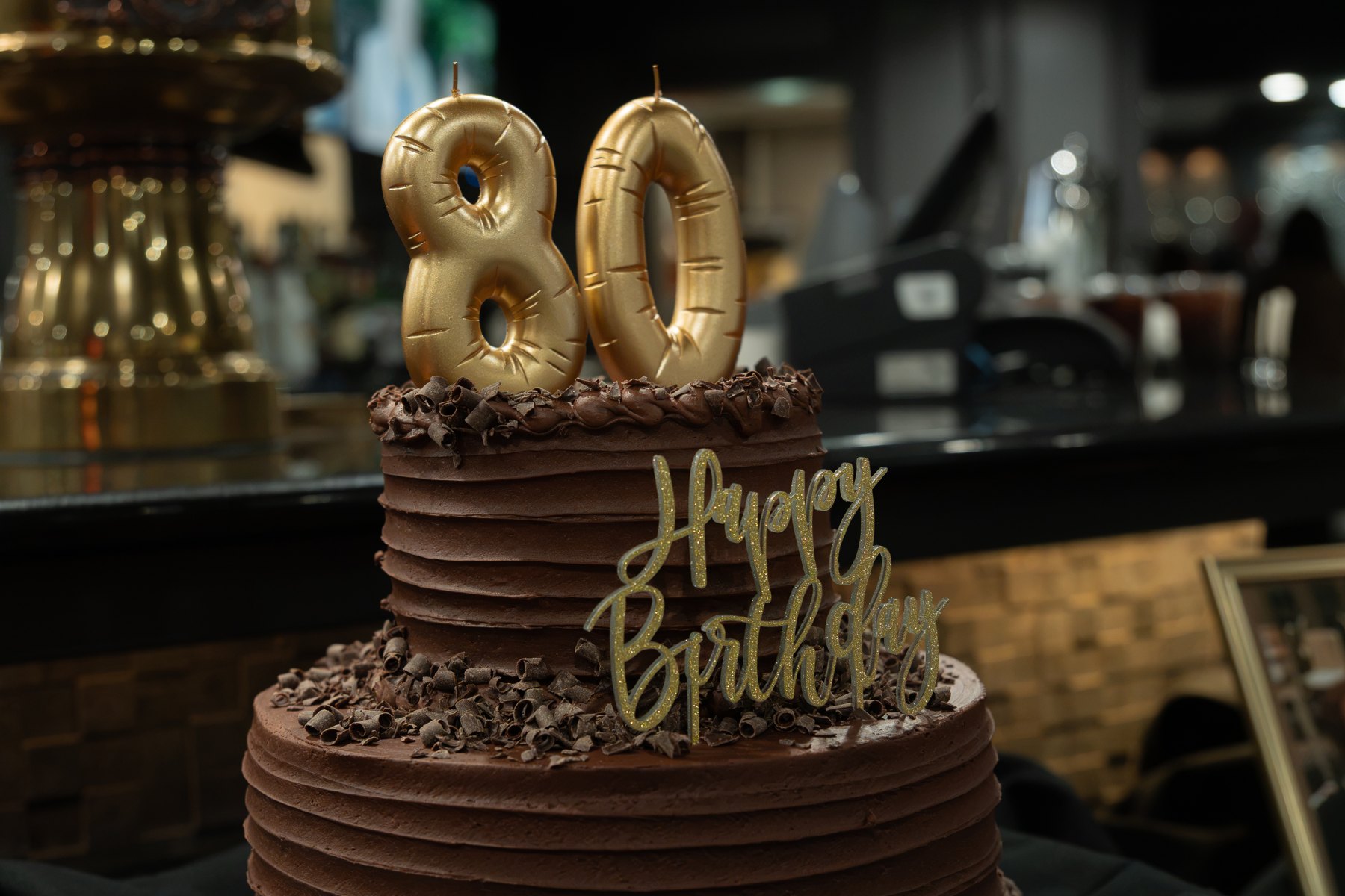 A chocolate birthday cake with gold 80 candles