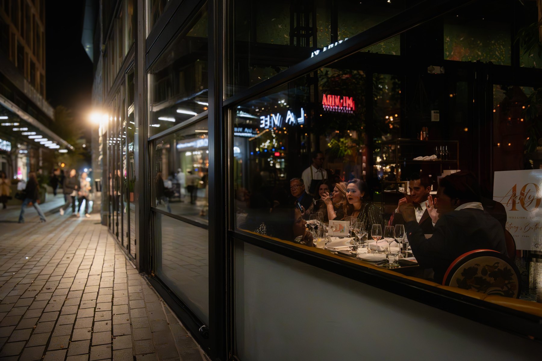 A view through the venue window of birthday guests gathered around a table